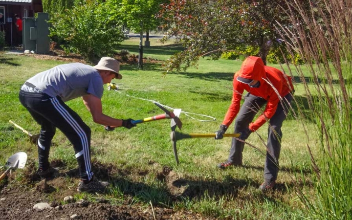 Two people use garden tools during a service project with outward bound